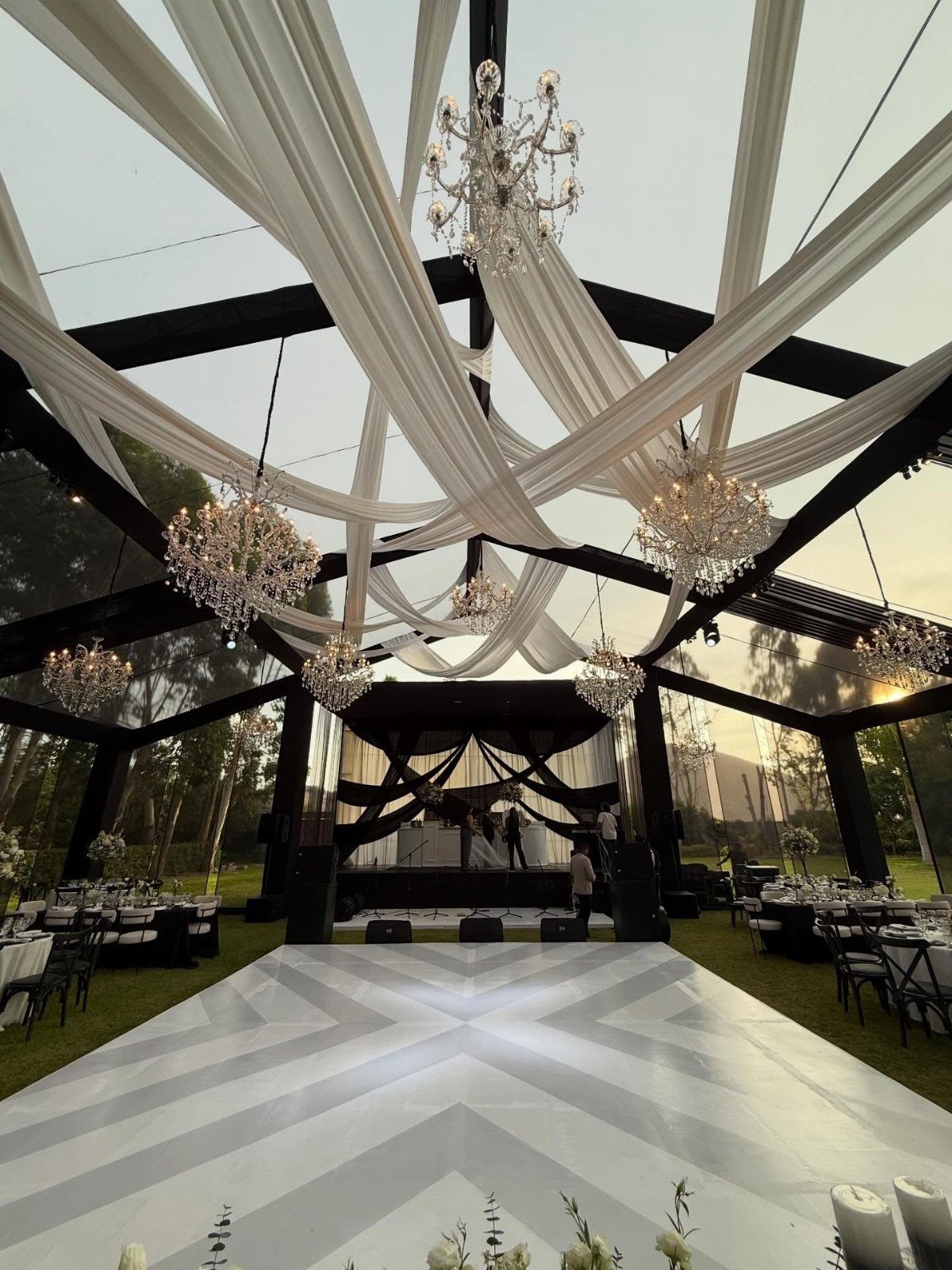 Outdoor wedding venue with black framing, white ceiling drapes, and geometric dance floor.
