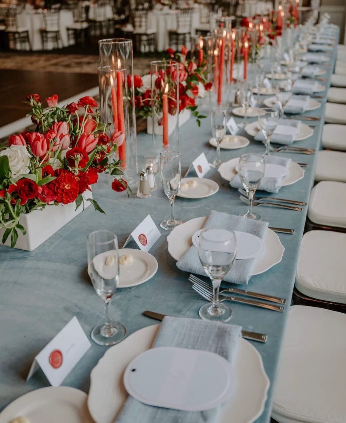 Wedding table setting with light blue linens, red flowers, and red taper candles.