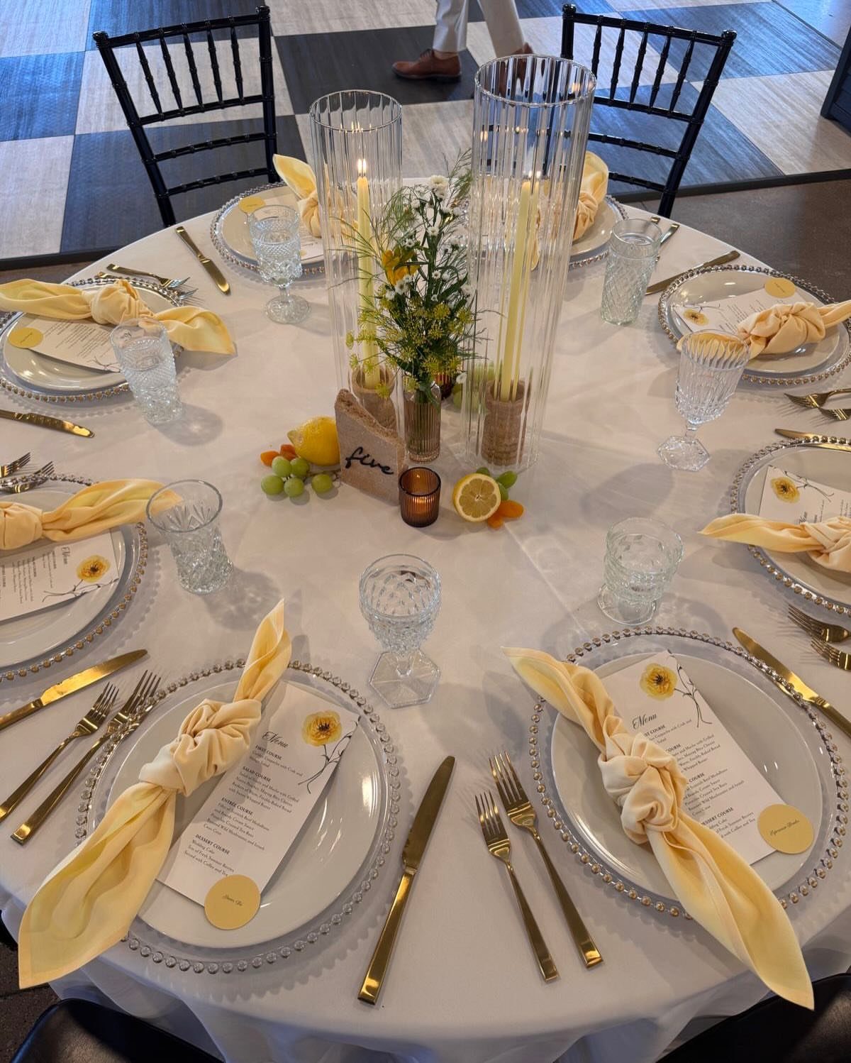 Wedding table setting with white linens, gold cutlery, and butter yellow napkins.