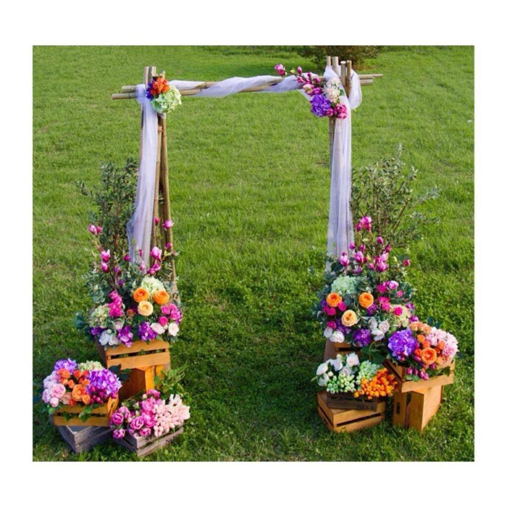 Wooden wedding arch decorated with white fabric and colorful flowers on green grass