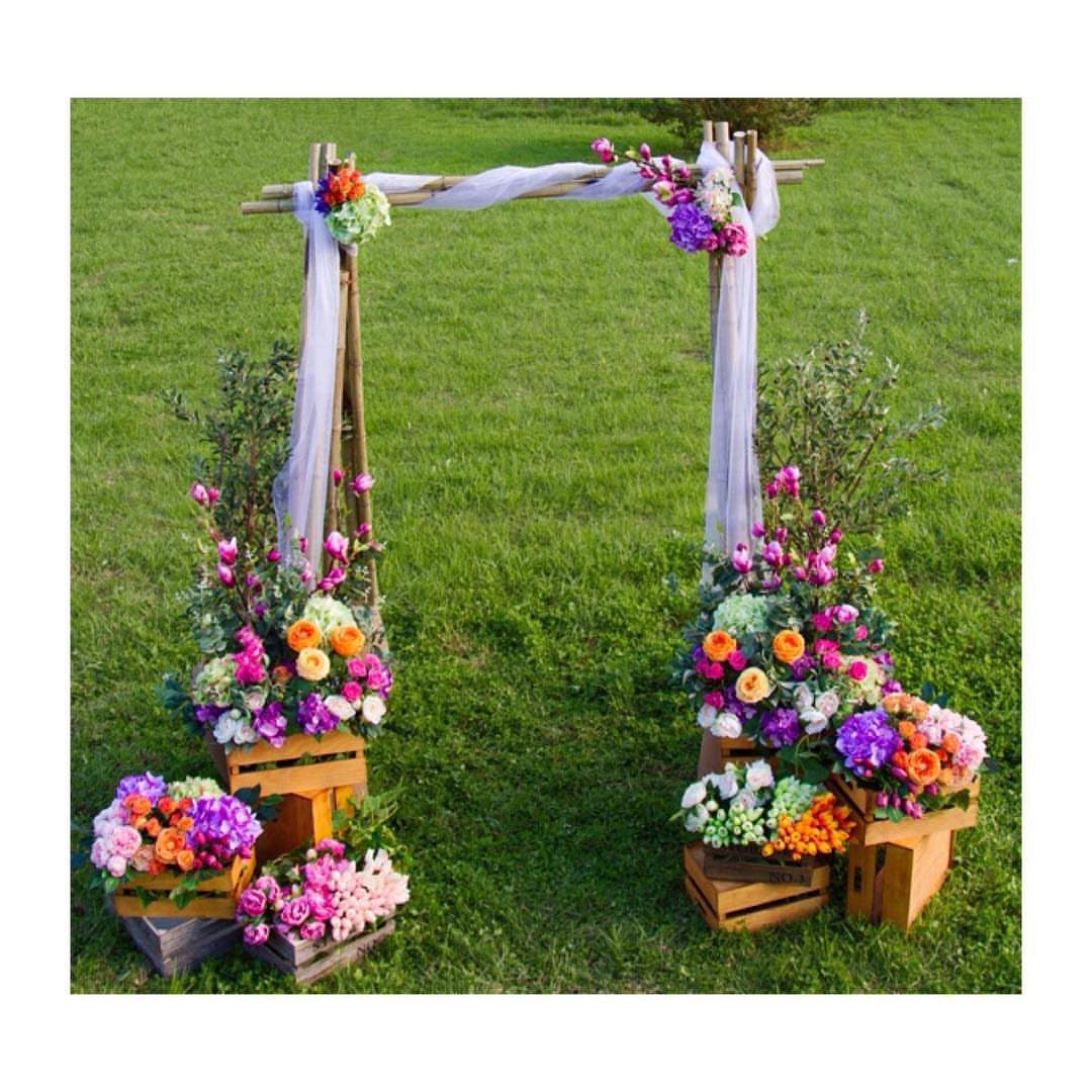 Wooden wedding arch decorated with white fabric and colorful flowers on green grass