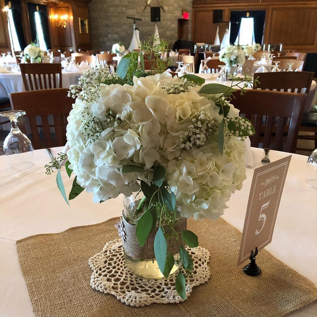 White hydrangea arrangement in a burlap-wrapped mason jar on a rustic table setting.