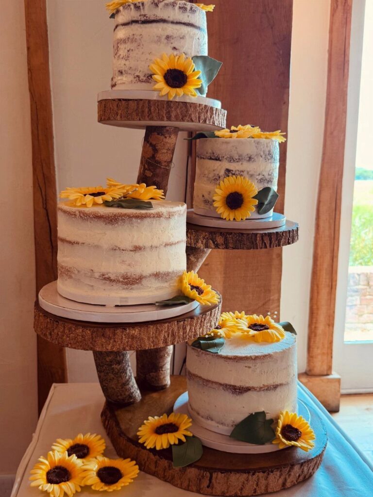 Three sunflower-decorated cakes on a tiered rustic wood log cake stand.