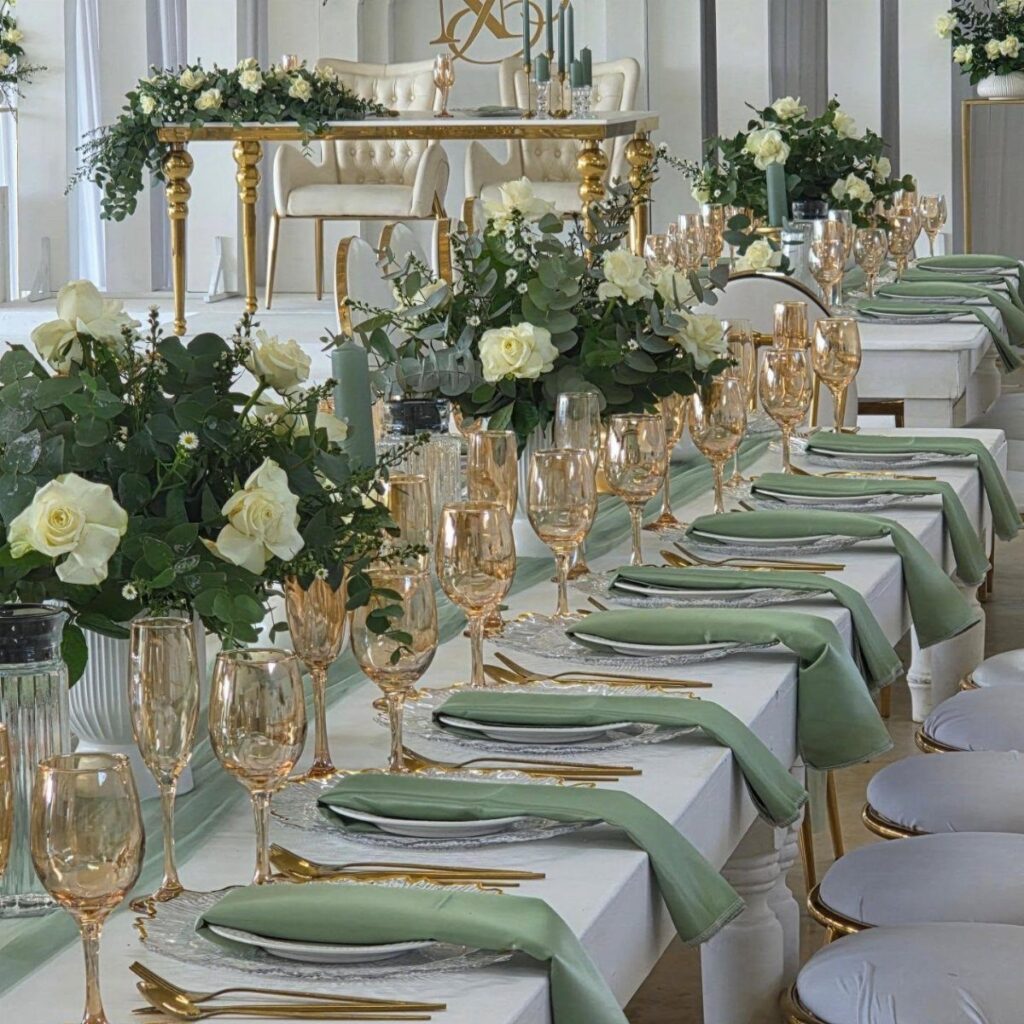 Wedding banquet table with white roses, sage green napkins, and gold accents.