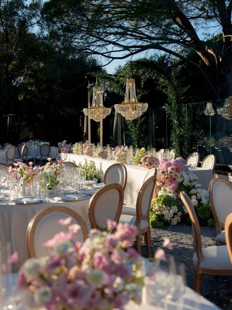 Outdoor wedding reception with pink and green floral centerpieces and crystal chandeliers.