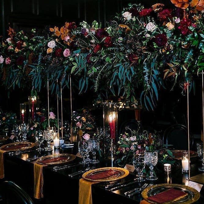 Elegant wedding table setting with black linens and a lush jewel-toned floral installation.