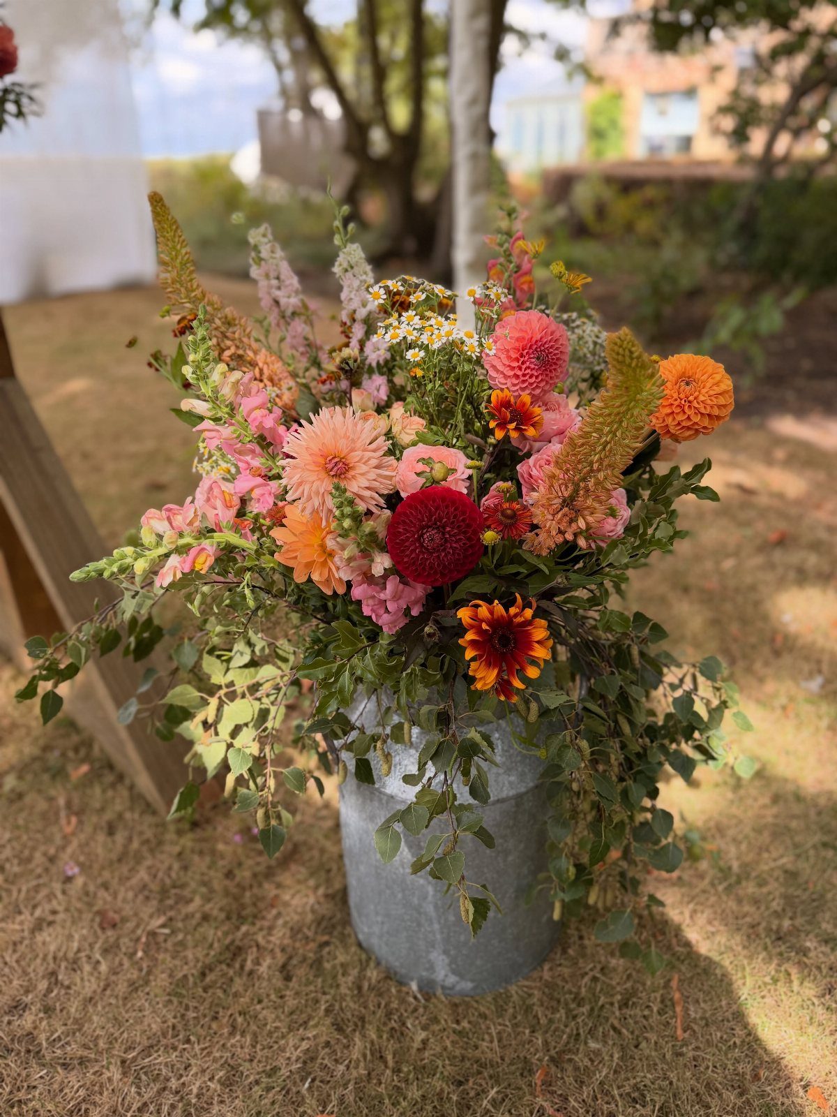 Floral arrangement with pink and orange dahlias in a metal bucket outdoors.