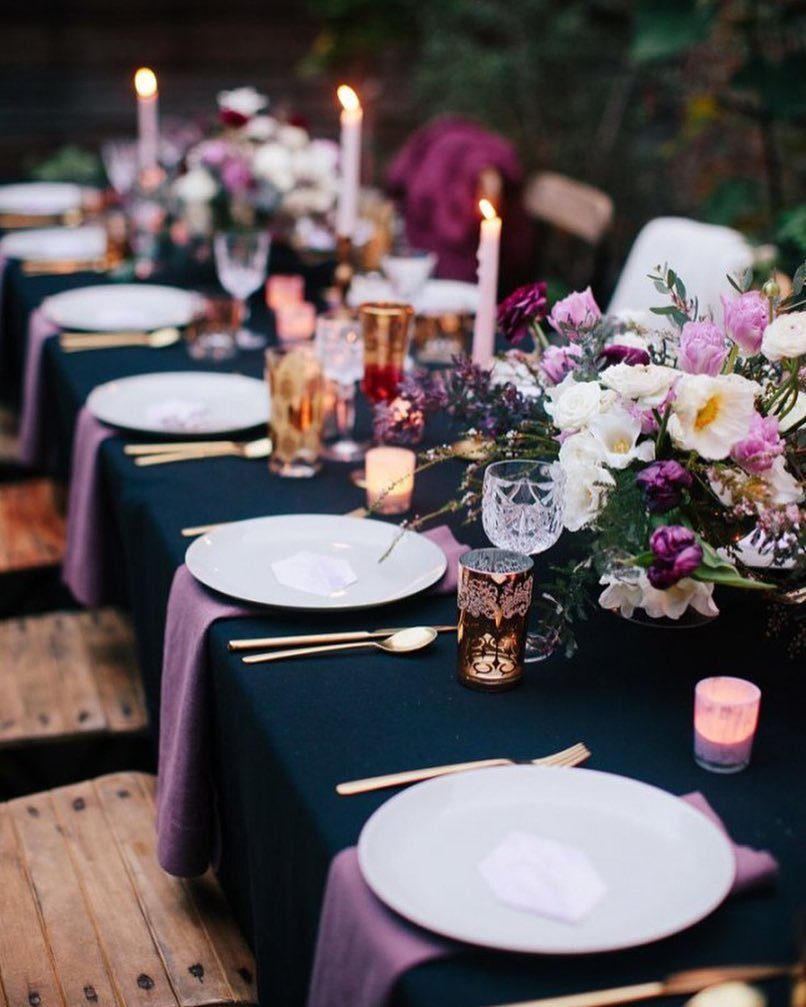 Navy blue table setting with lilac napkins, gold cutlery, and purple floral centerpieces.