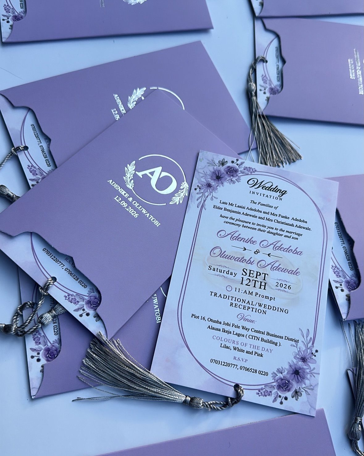 Purple wedding invitation suite with floral borders and silver tassels on white background