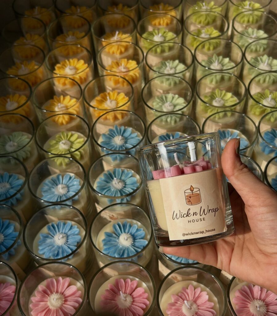 Hand holding a branded scented candle surrounded by colorful flower-shaped wax candles.