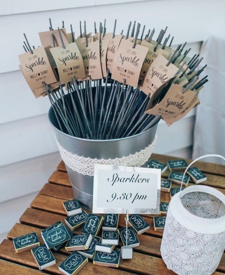 Silver bucket of sparklers with tags, matchboxes, and a sign on wooden table