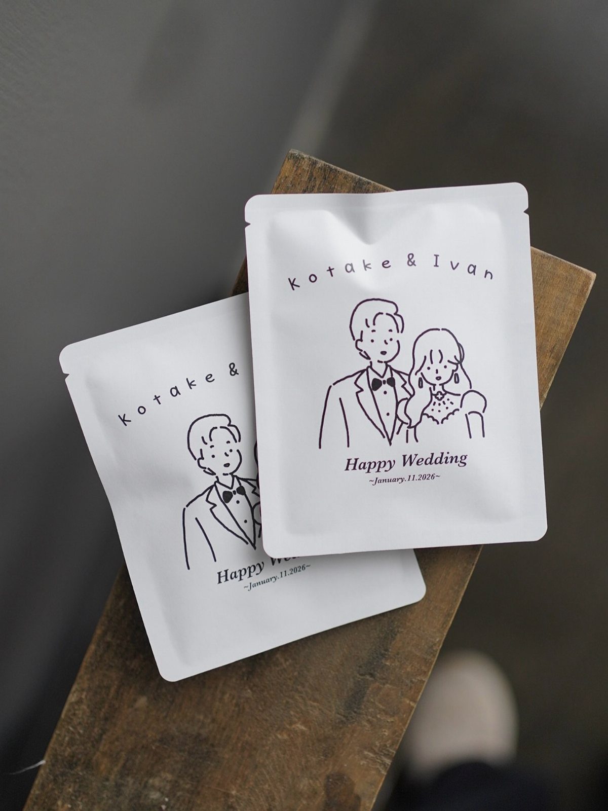 Two white wedding favor sachets with a minimalist couple illustration on wooden surface