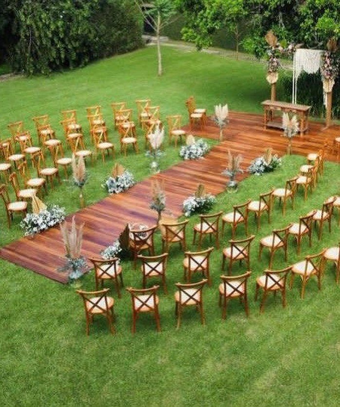 Wooden cross-back chairs arranged in rows along a wooden aisle on green grass.
