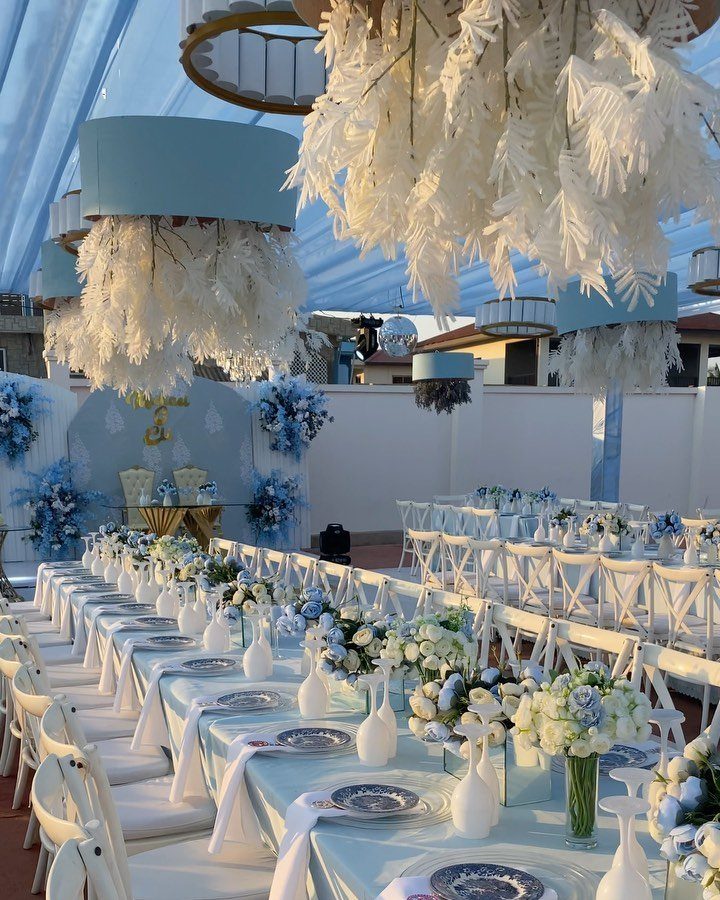 Wedding reception tables with light blue linens, white chairs, and blue floral centerpieces.