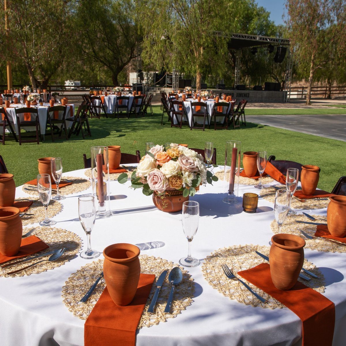 Wedding table setting with white linens, terracotta napkins, clay cups, and peach florals.