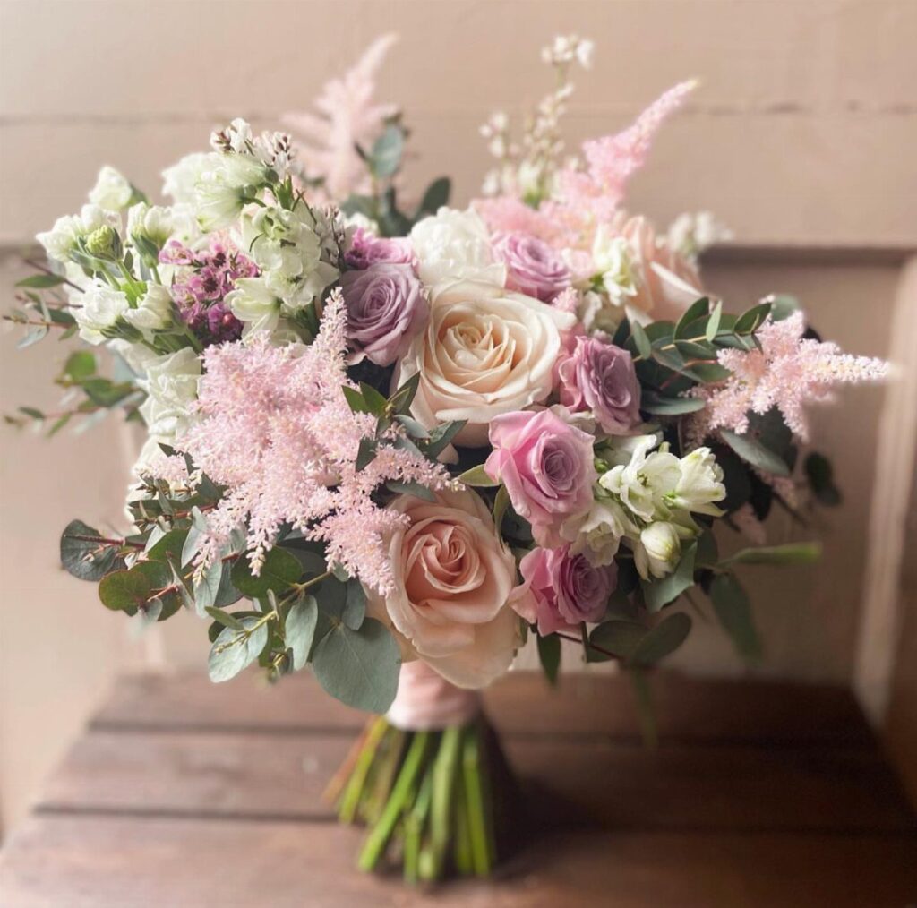 Blush pink and lavender rose bouquet with greenery on a wooden table