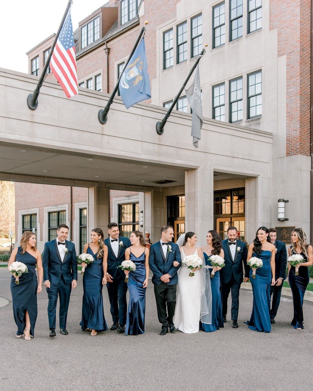 Wedding party walking outdoors with bridesmaids and groomsmen wearing navy blue attire.