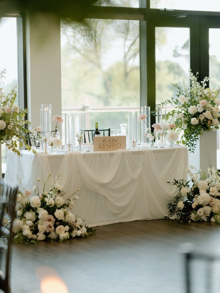 Decorated wedding head table with white linens, blush flowers, and glass vases.