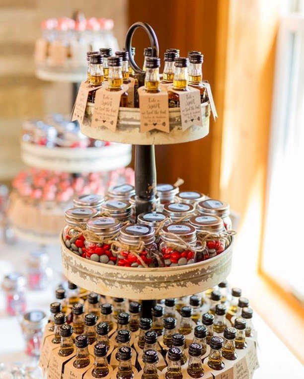Three-tiered wooden display stand holding small favor bottles and jars of candy.