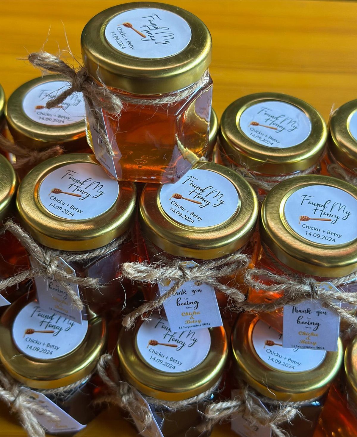 Small hexagonal honey jars with gold lids and twine bows for wedding favors.