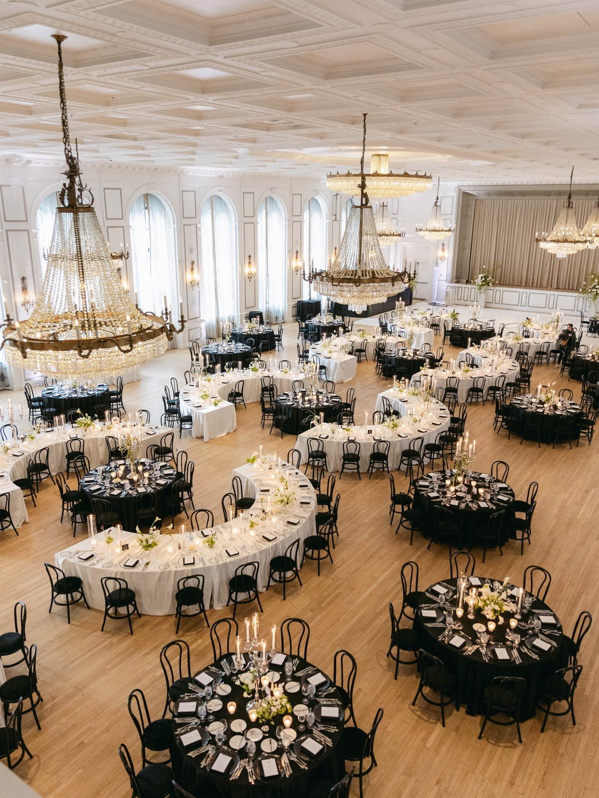 Grand ballroom with a mix of round and curved wedding tables and chandeliers.