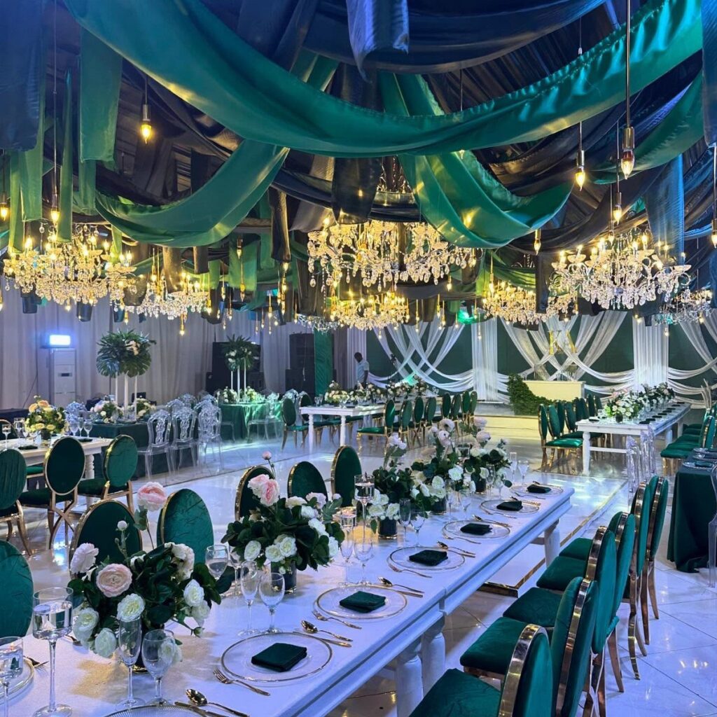 Wedding reception hall with emerald green ceiling drapes, velvet chairs, and white floral centerpieces.